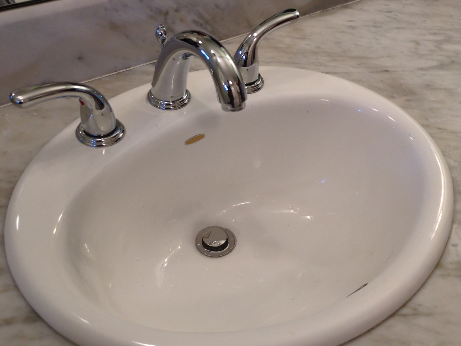 Chrome three-piece bathroom faucet with curved lever handles on a white oval sink set into a gray-veined marble counter