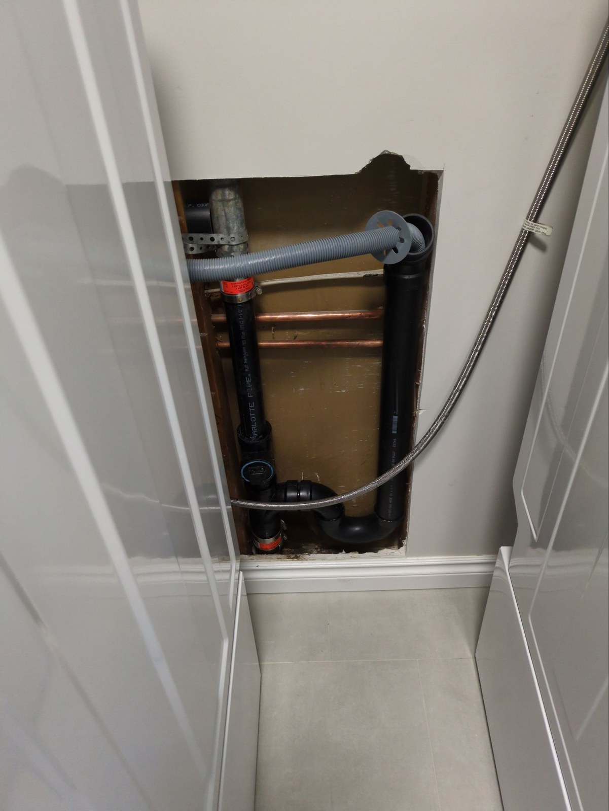New black ABS laundry drain inside an opened wall, with a P-trap at the bottom, a capped cleanout on the riser and copper supply lines behind