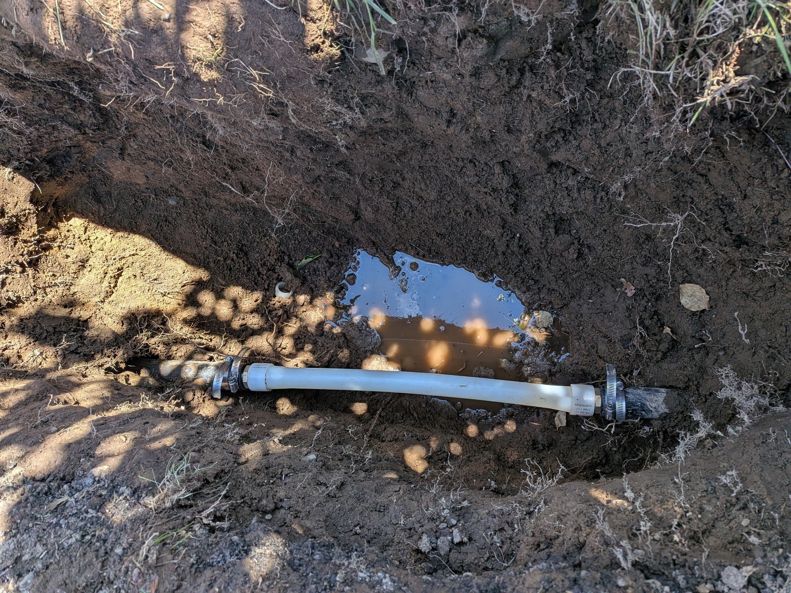 New polyethylene section clamped into a buried water service line at the bottom of an open trench with groundwater seeping in